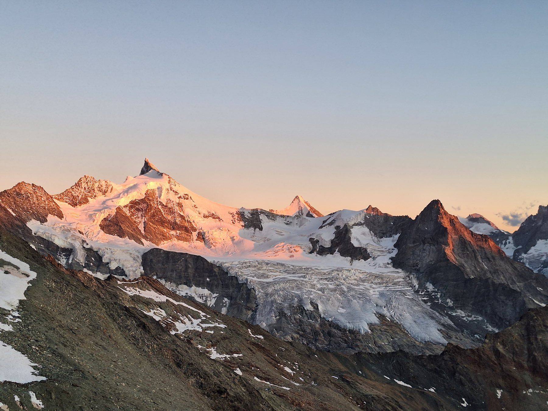 Avondlicht kleurt een besneeuwde bergkam roze en oranje.